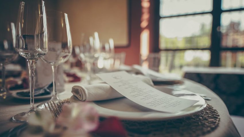 A cozy indoor fine dining table setup with elegant tableware and a stylish menu under warm lighting.